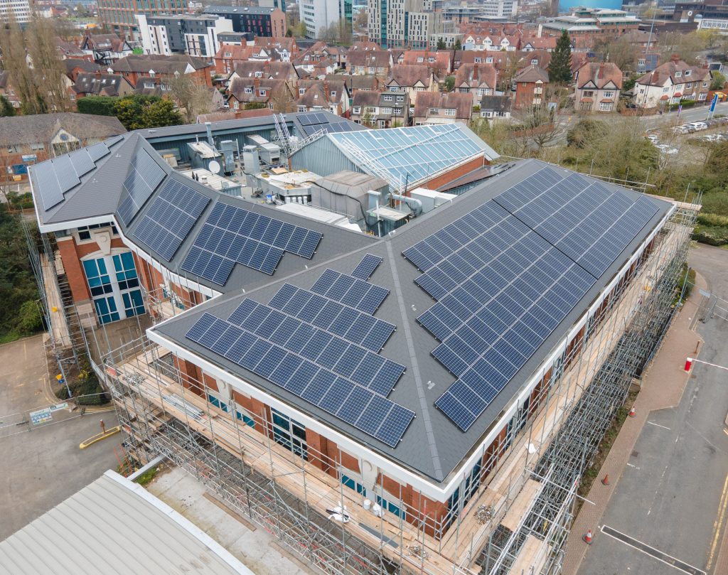 Large building with solar panels installed on the roof with scaffolding around the building.