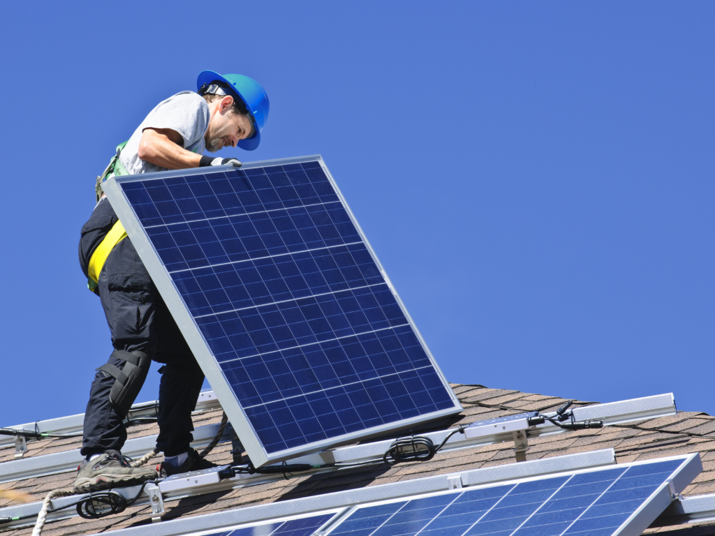 A man installing solar panels on the roof of a house.