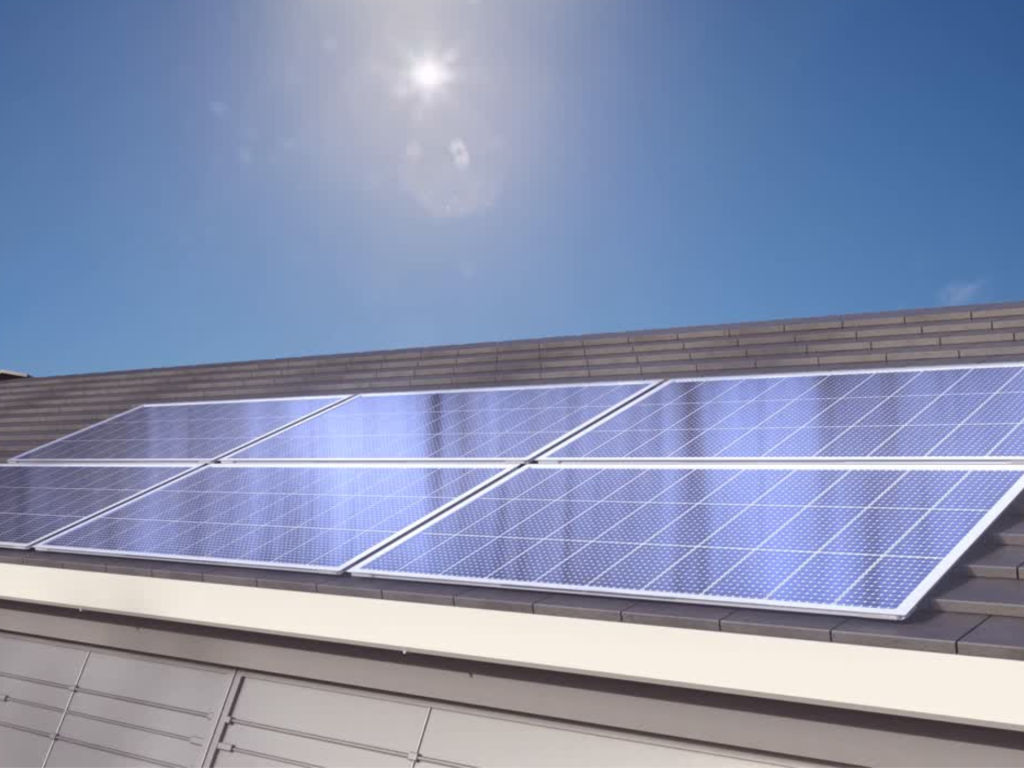 Image of solar panels on a roof with blue skies and the sun shining in the background.