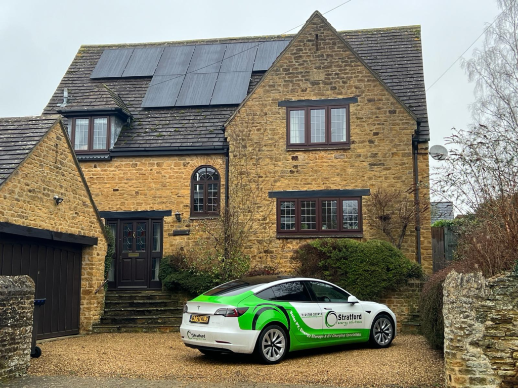 A Stratford Energy Solutions electric vehicle parked in front of a house with solar panels installed on the roof.